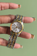 A gold and silver wristwatch with a metallic band and a floral pattern on the dial, held in a person's hand.