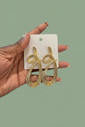 Gold snake-shaped earrings on a white card held by a hand with a blurred background