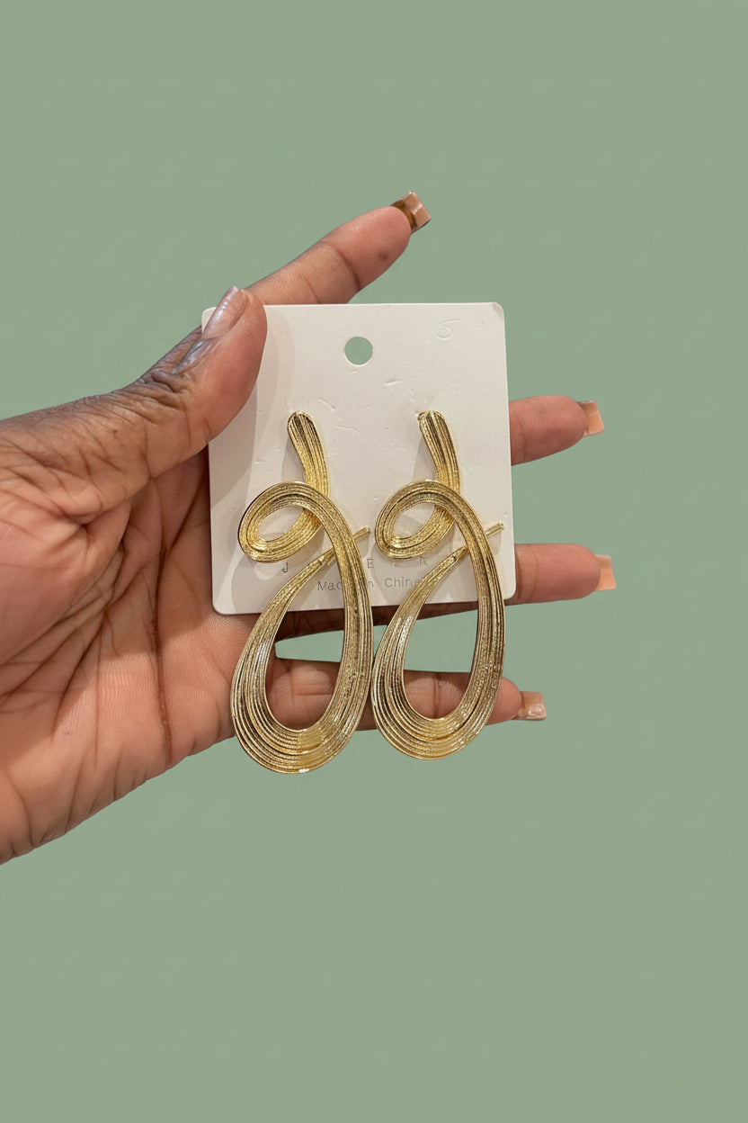 Gold snake-shaped earrings on a white card held by a hand with a blurred background